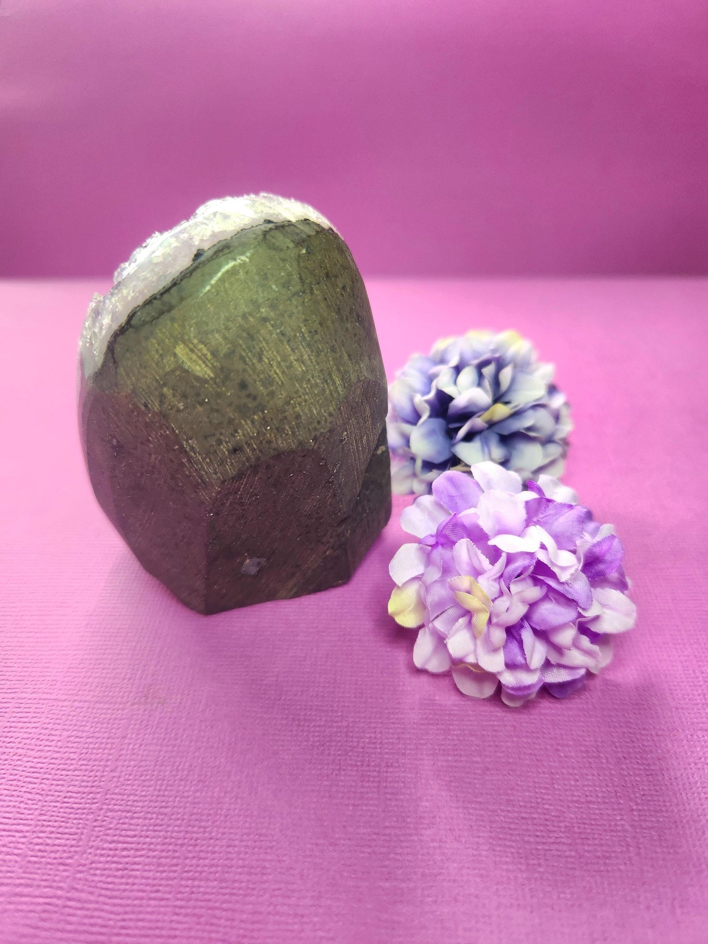 Back view of Amethyst Cluster Cut Base showing natural brown matrix and crystal base on a purple background with two flower props. Raw amethyst geode with exposed host rock, perfect for crystal collectors, meditation, energy healing, and spiritual décor.