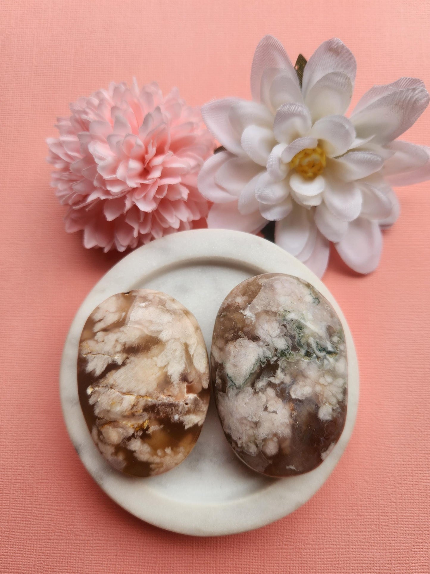 Flower agate palmstone displayed in a white ceramic dish with two floral props on a soft pink background, featuring polished natural flower agate crystal with floral inclusions, healing gemstone palm stone for growth manifestation calm and emotional balance, metaphysical crystal perfect for gifting meditation altar decor and crystal collections