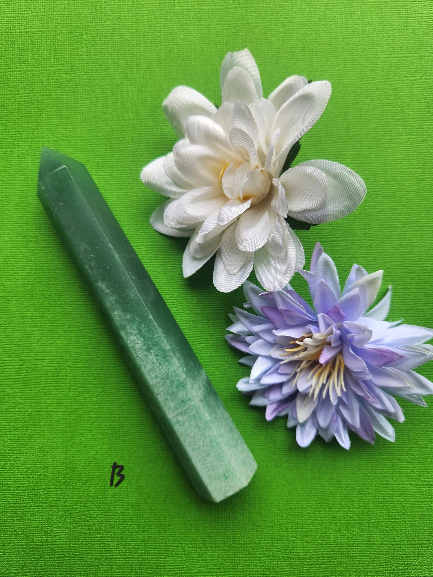 Green aventurine crystal tower B photographed upright on a green background with floral props showing smooth green stone patterns polished crystal point for home decor and metaphysical use