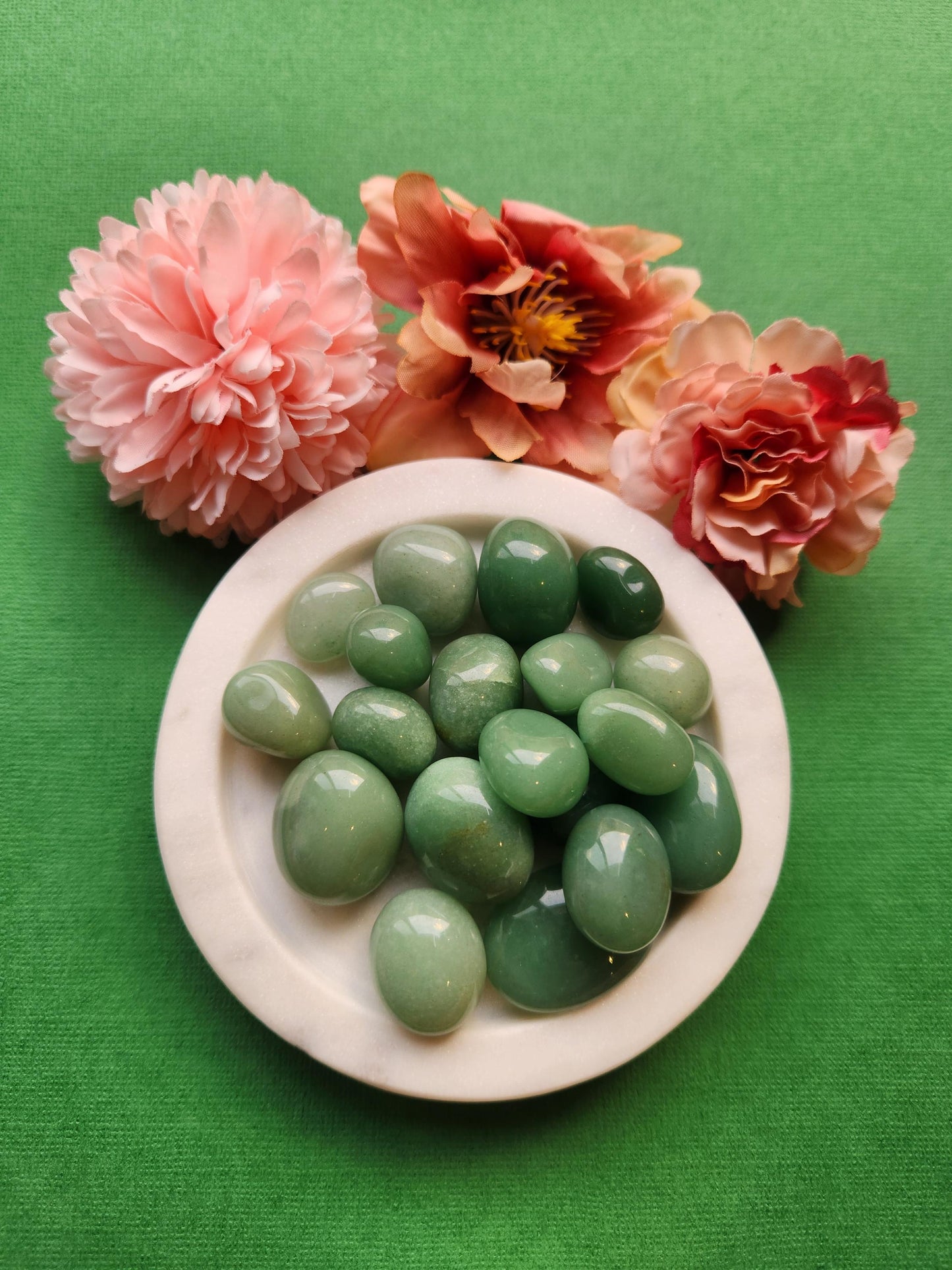 Polished Green Aventurine tumbled stones displayed on a green background. These natural healing crystals are known for attracting luck, abundance, and prosperity. Perfect for meditation, chakra balancing, energy work, and spiritual healing. Ideal for use in crystal grids, wellness rituals, or as meaningful gifts for crystal lovers. Soothing green tones support emotional calm and heart chakra alignment.