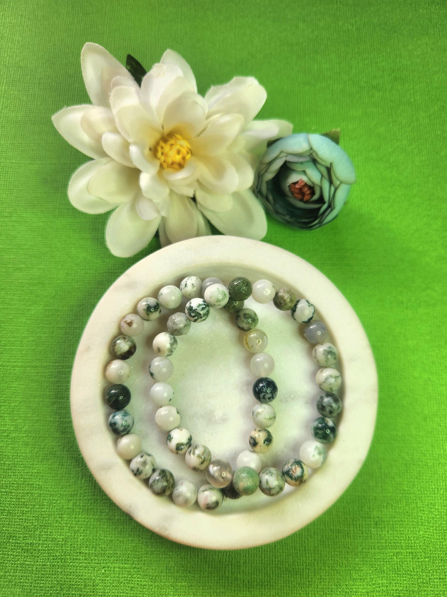 Natural Moss Agate 8mm crystal bracelets shown in a white dish with decorative flower props against a green background, polished moss agate bead bracelets for grounding new beginnings prosperity and mindful gifting