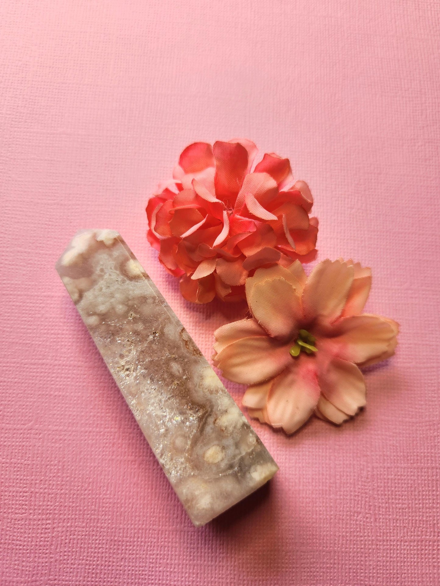 Side view of a polished Pink Amethyst crystal tower with two flower props on a light pink background, showcasing unique natural patterns, heart chakra healing stone, perfect for meditation, spiritual altar décor, and crystal collectors.
