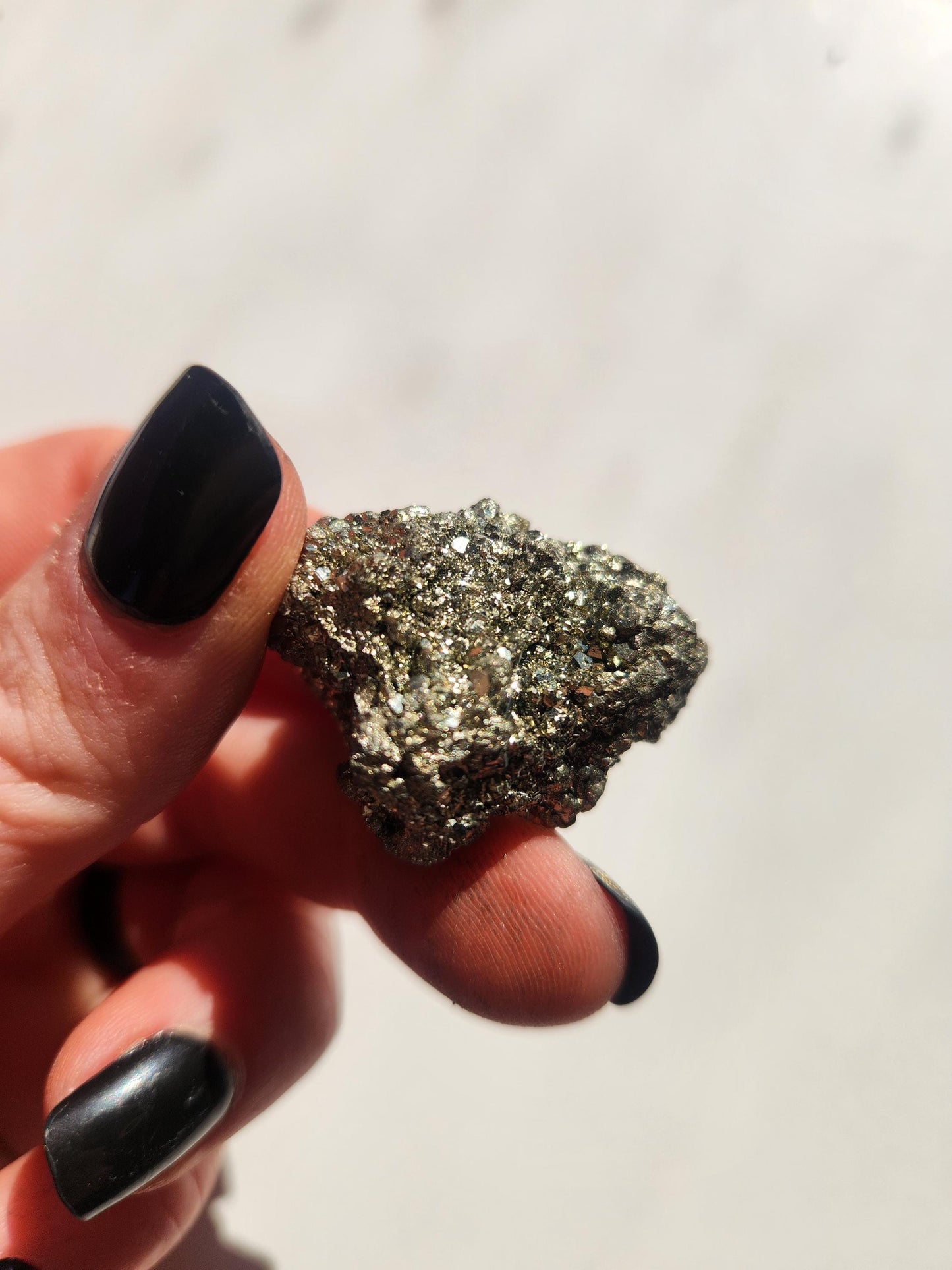 Hand holding raw Pyrite crystal pieces in sunlight against a white background. The metallic gold stones sparkle naturally. Perfect for abundance, manifestation, and crystal decor