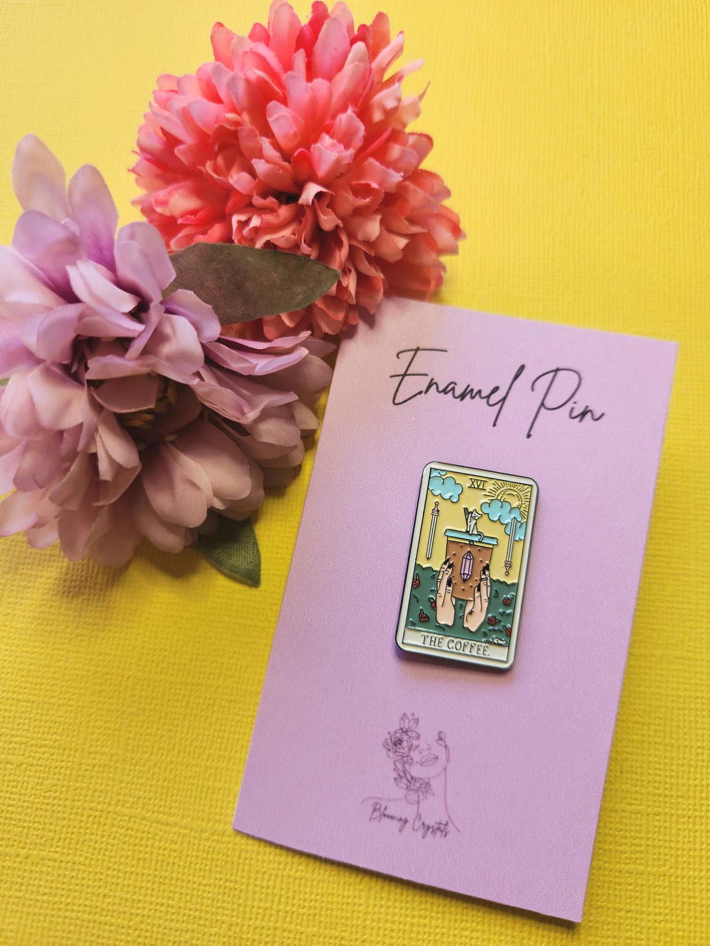 Enamel pin designed as a traditional tarot card featuring an iced coffee illustration, styled with two flowers on a bright yellow backdrop — perfect for coffee lovers, tarot fans, and enamel pin collectors.