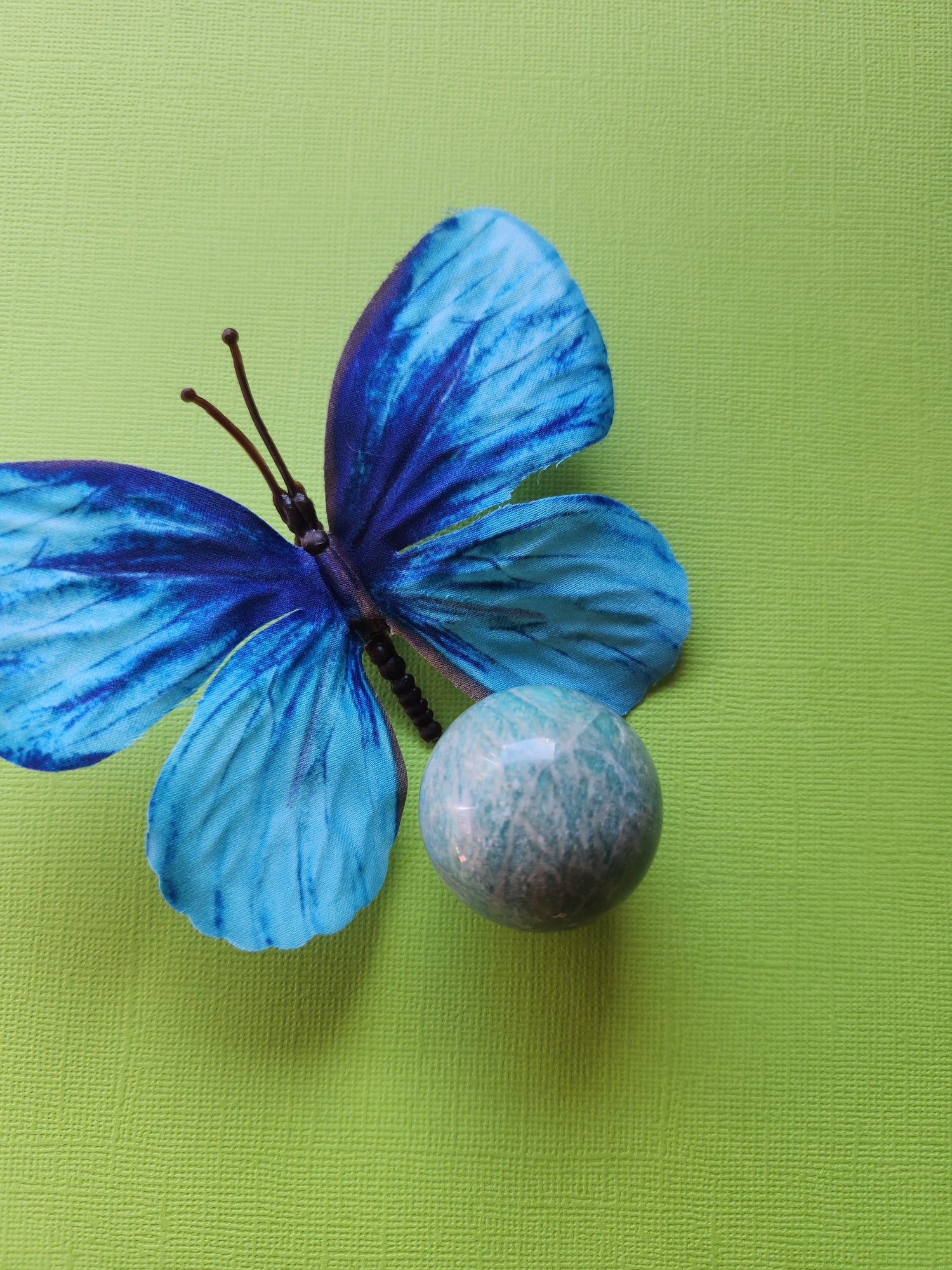 Amazonite sphere crystal with blue butterfly on bright green background – polished healing stone for balance and calming energy.
