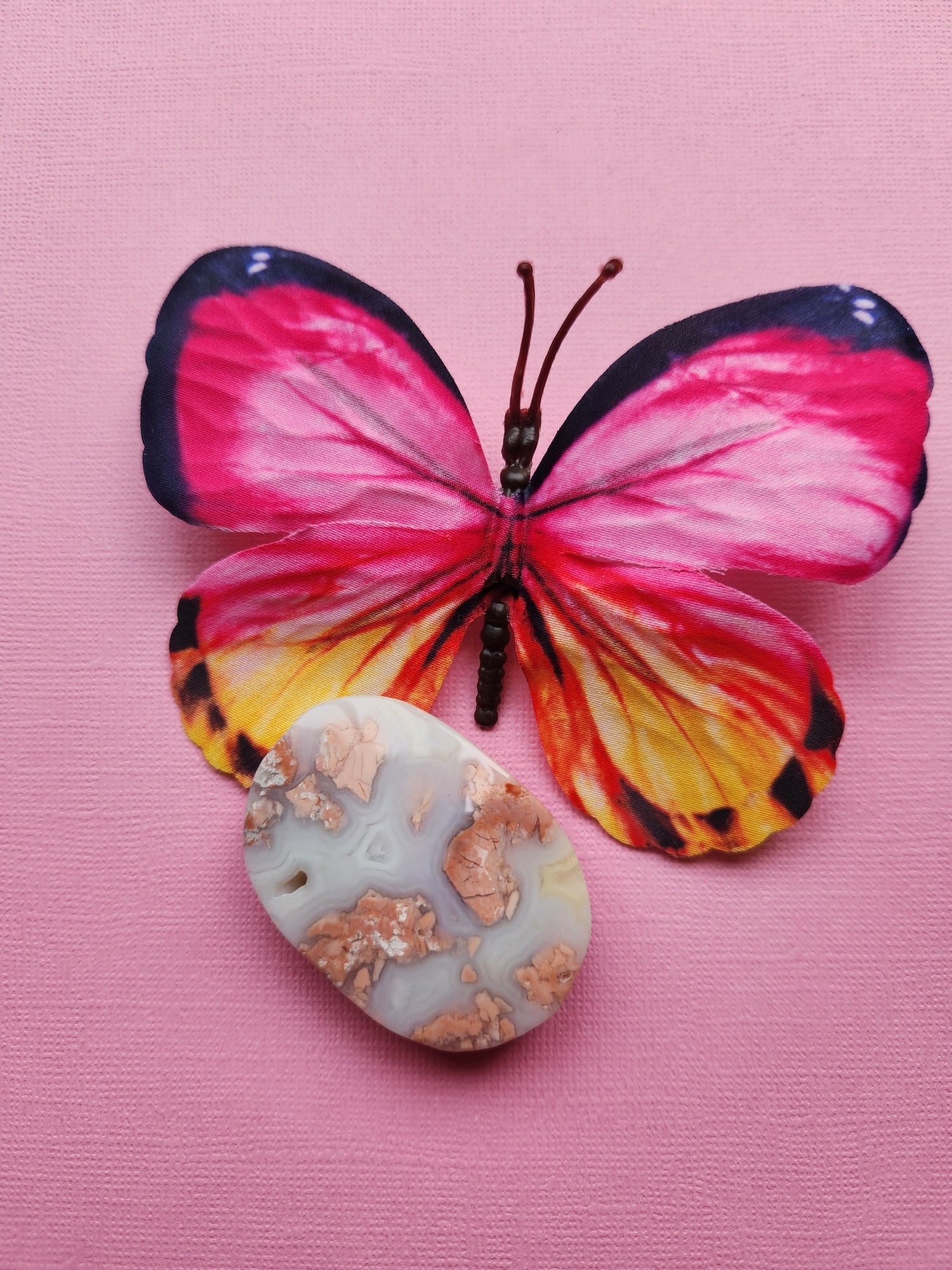 Pink cotton candy agate palmstone with pink and yellow butterfly with black details on light pink background – polished healing crystal for meditation and energy.