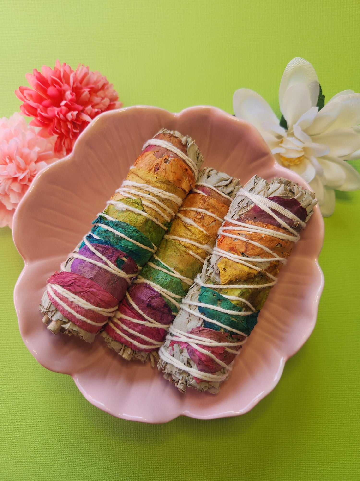 White sage sticks with colorful chakra petals in a pink flower bowl on bright green background – smoke cleansing and smudging tools from Australian crystal shop
