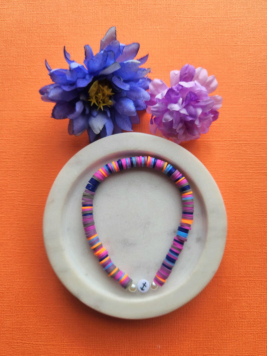 Sagittarius zodiac clay beaded bracelet in white dish with two flower props on orange background, handmade purple blue orange dark purple light blue beaded astrology bracelet with Sagittarius symbol bead, stretchy elastic zodiac jewellery product photo