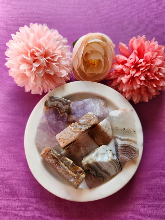 Raw crystal specimen combining Amethyst and Crazy Lace Agate in one natural formation. This unique unpolished stone features deep purple Amethyst growing alongside banded Crazy Lace Agate with cream, gold, and red tones. Ideal for healing, grounding, spiritual work, altar decor, or crystal grids. The one-of-a-kind fusion of minerals creates stunning texture and contrast, shown on a purple background in natural light to highlight raw edges and rich color variation.