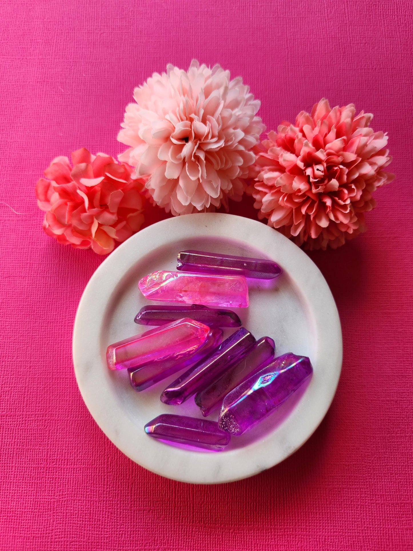 Pink and purple aura quartz rough points displayed on a soft pink background, showcasing their vibrant iridescent colors and natural crystal formations. These raw crystals are prized for their spiritual energy, healing properties, and chakra balancing. Perfect for meditation, Reiki practices, and energy work. The pink backdrop enhances the stones' luminous hues, making them ideal for crystal collectors and holistic wellness enthusiasts.