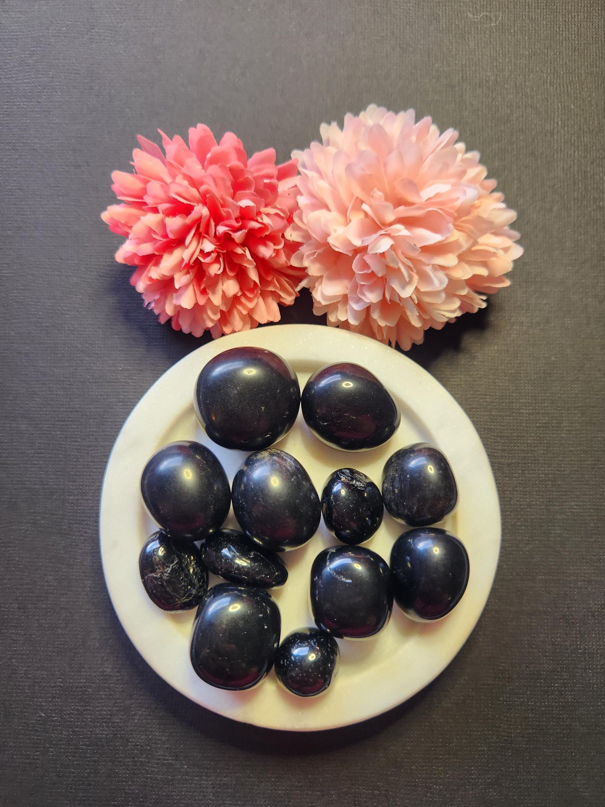 Black Obsidian tumbled stones displayed on a black background, showcasing their smooth, glossy surface and deep volcanic glass appearance. These small, palm-sized crystals are ideal for grounding, spiritual protection, and Root Chakra work. Each stone features subtle natural variations and a reflective finish. The dark background highlights the rich black tones and polished texture of the Obsidian, perfect for crystal healing, pocket stones, or ritual tools.