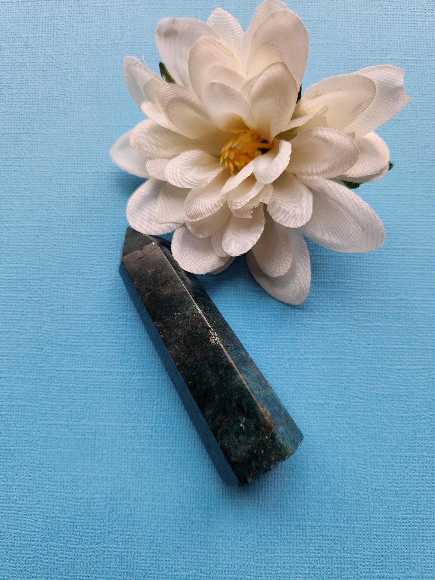 Close-up of a single Blue Apatite crystal tower on a blue background. This natural crystal point showcases deep blue color, smooth polished surfaces, and distinct natural lines. Known for enhancing communication and creativity, it’s used in meditation and healing rituals. The blue background complements the crystal’s vibrant tones, emphasizing clarity and intricate details for collectors and spiritual practitioners.