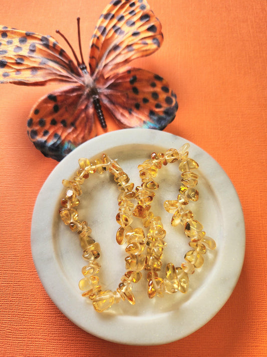 Citrine chip bracelet with golden yellow crystal chips displayed in a white dish with an orange butterfly prop and bright orange background. Heat treated citrine crystal bracelet symbolizing abundance, joy, and confidence. Handmade stretch gemstone bracelet for positivity and manifestation, perfect for crystal healing, jewelry stacking, and boho style photography.