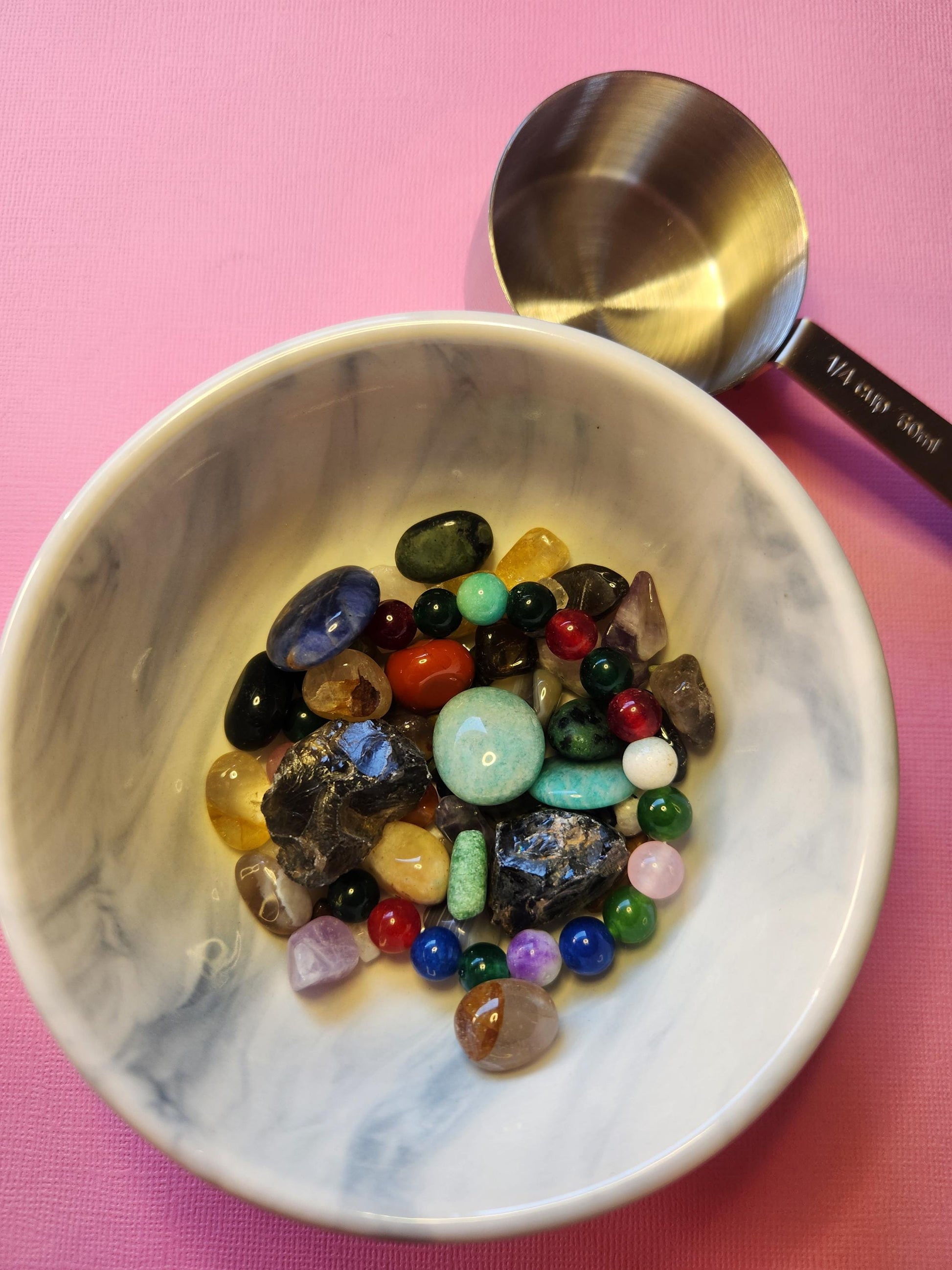 Flat lay image of a Crystal Confetti scoop on a soft pink background, displaying tumbled and raw gemstones in a surprise assortment. Great for intention setting, meditation tools, or adding to your crystal collection. Each scoop is unique and may include stones for love, abundance, protection, and clarity. Perfect for gifting or witchy subscription box fillers.