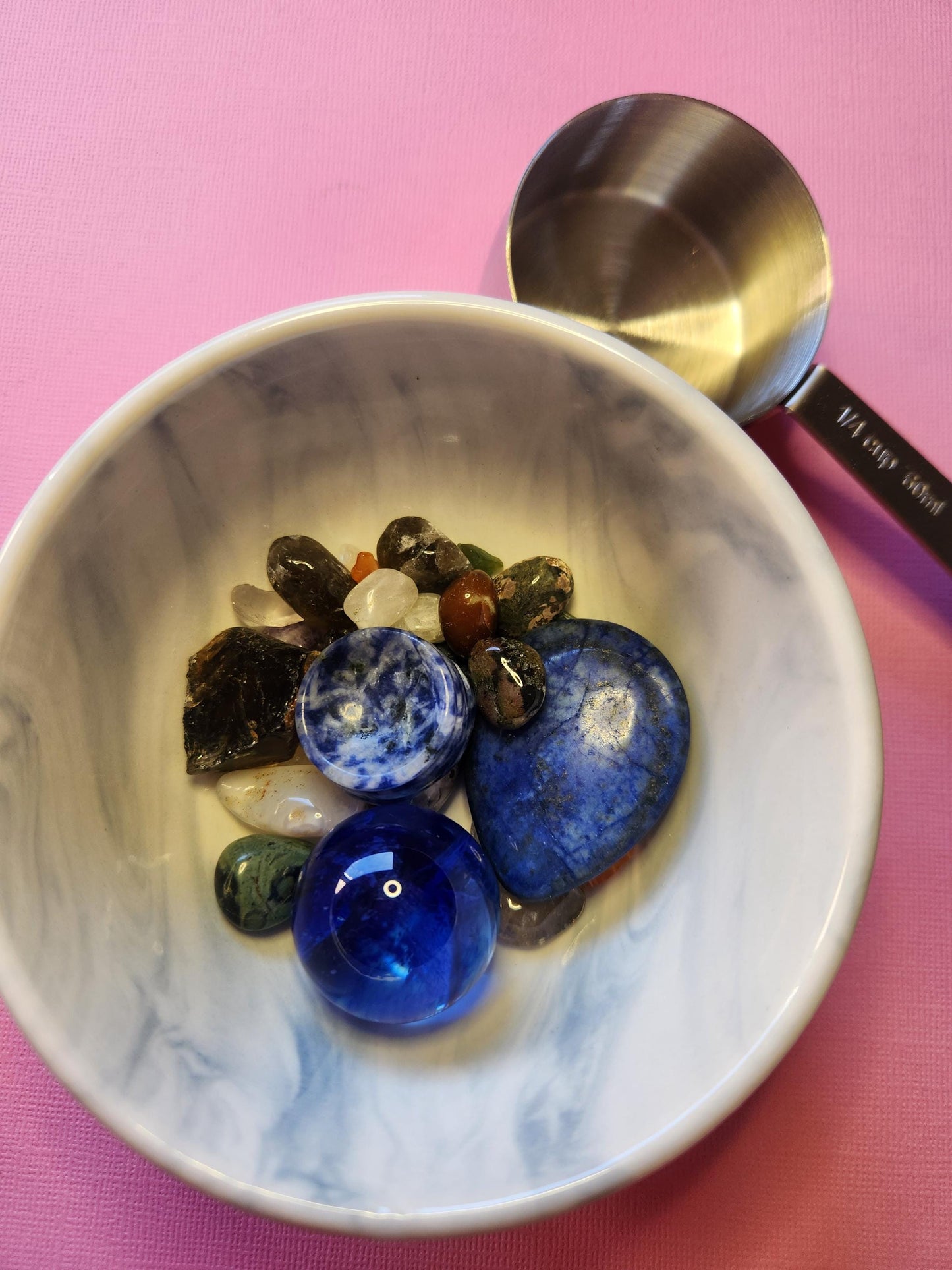 Assorted crystal confetti scoop displayed on a pink background, filled with a variety of healing stones and chips. Each scoop is a unique blend of high-vibe stones that could support love, protection, clarity, or creativity. Great for those who enjoy collecting crystals, using them in rituals, or gifting to friends who love spiritual tools and surprise crystal mixes.