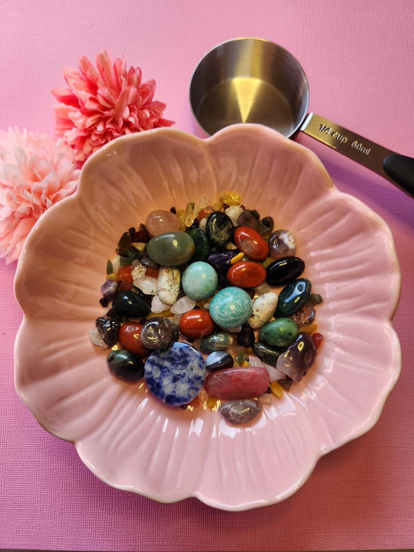 Close-up of a Crystal Confetti scoop on a pink background, containing a random mix of polished and raw crystals. Includes potential stones like Aventurine, Fluorite, and Citrine. Ideal for use in spiritual rituals, crystal grids, or as a fun metaphysical gift. The mix highlights color variety and energetic potential, with pink backdrop adding a playful, magical vibe.
