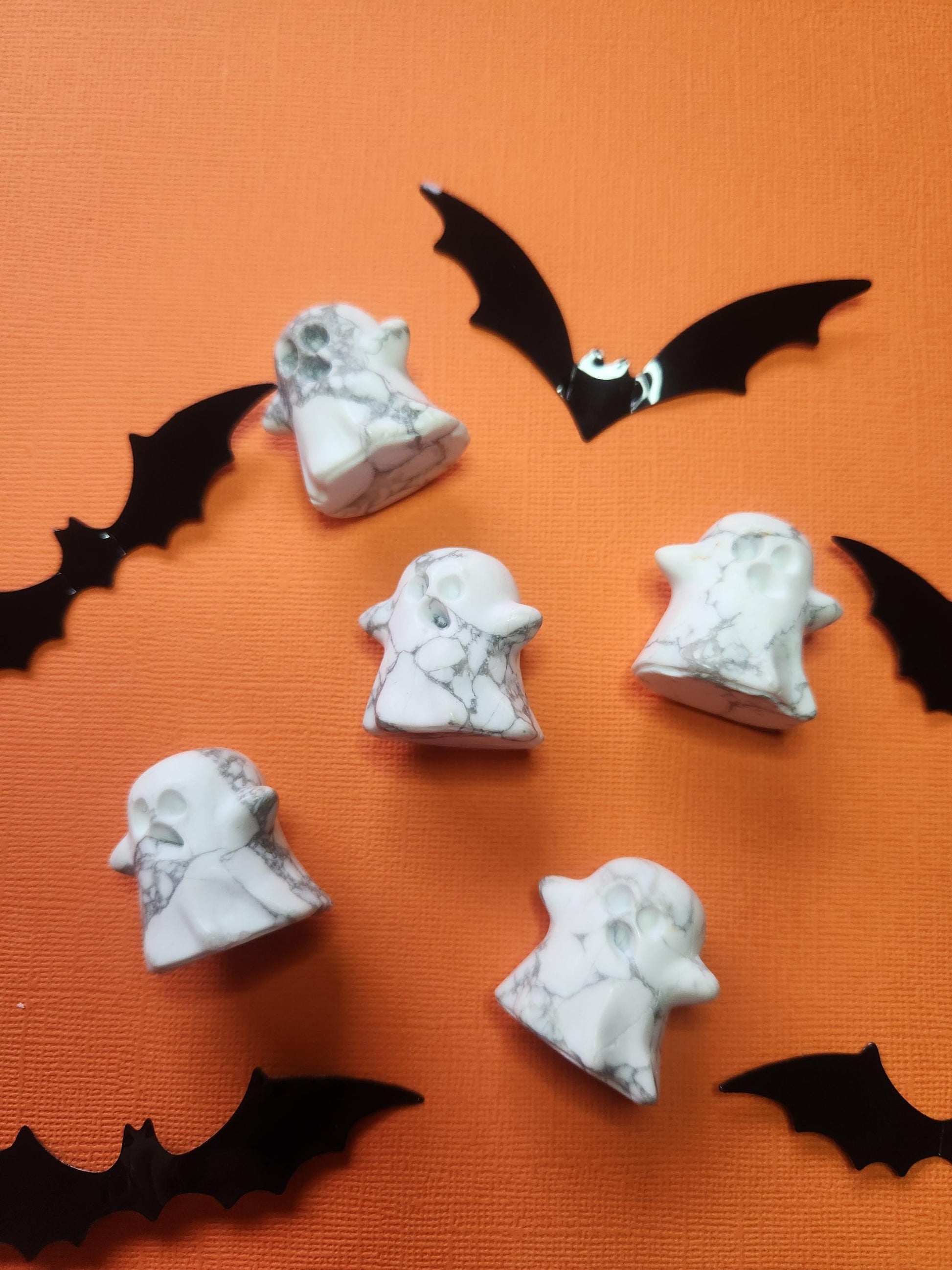 Close-up flat lay of a white howlite ghost crystal on an orange background, with black bat decorations for a spooky Halloween aesthetic.