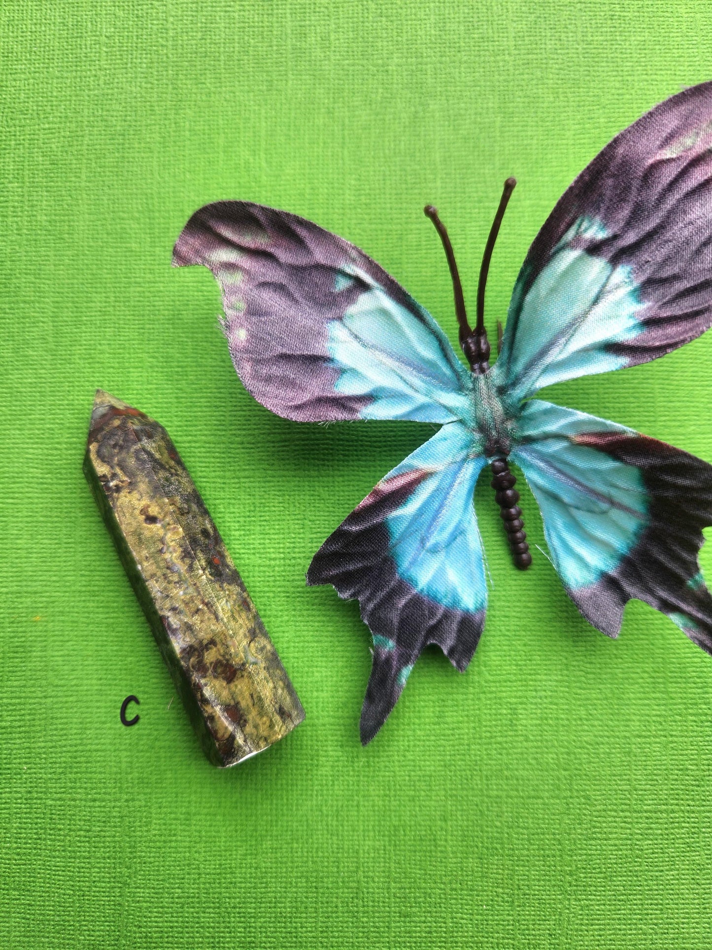 Dragons Bloodstone Tower B displayed with butterfly prop on green background, polished red and green jasper crystal tower, courage and strength stone for grounding energy, motivation, root chakra healing, witchcraft supplies, meditation crystals, and high-vibe gemstone décor