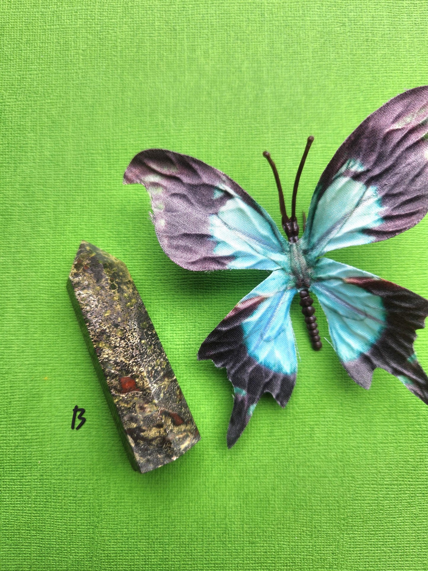 Dragons Bloodstone Tower B displayed with butterfly prop on green background, polished red and green jasper crystal tower, courage and strength stone for grounding energy, motivation, root chakra healing, witchcraft supplies, meditation crystals, and high-vibe gemstone décor