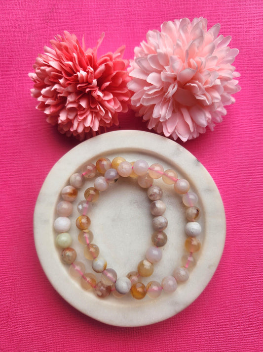 Two flower agate 8mm beaded bracelets displayed in a white dish on a pink background with soft flower props featuring polished crystal beads for growth confidence self love emotional healing energy bracelet and gift