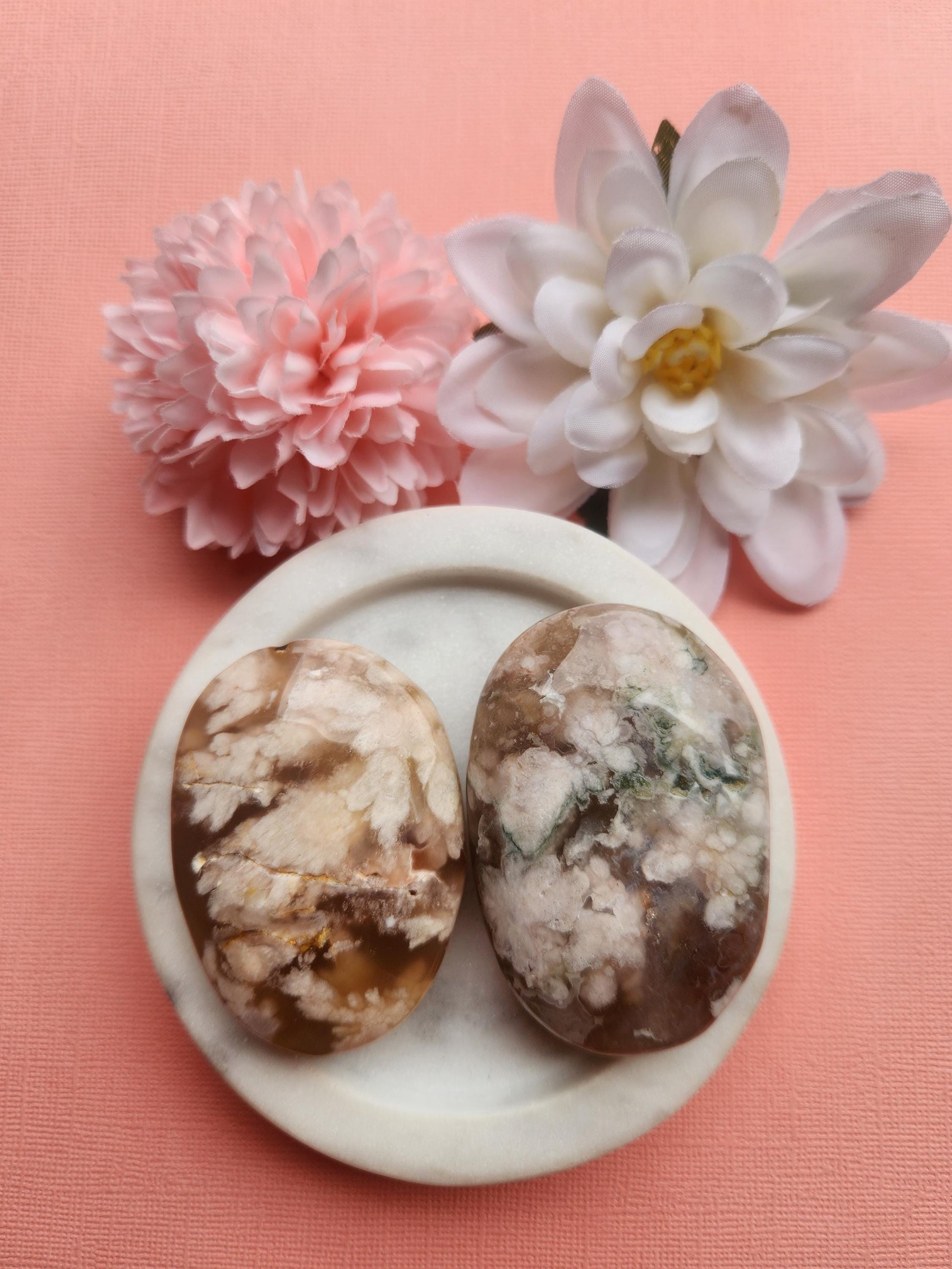 Flower agate palmstone displayed in a white ceramic dish with two floral props on a soft pink background, featuring polished natural flower agate crystal with floral inclusions, healing gemstone palm stone for growth manifestation calm and emotional balance, metaphysical crystal perfect for gifting meditation altar decor and crystal collections