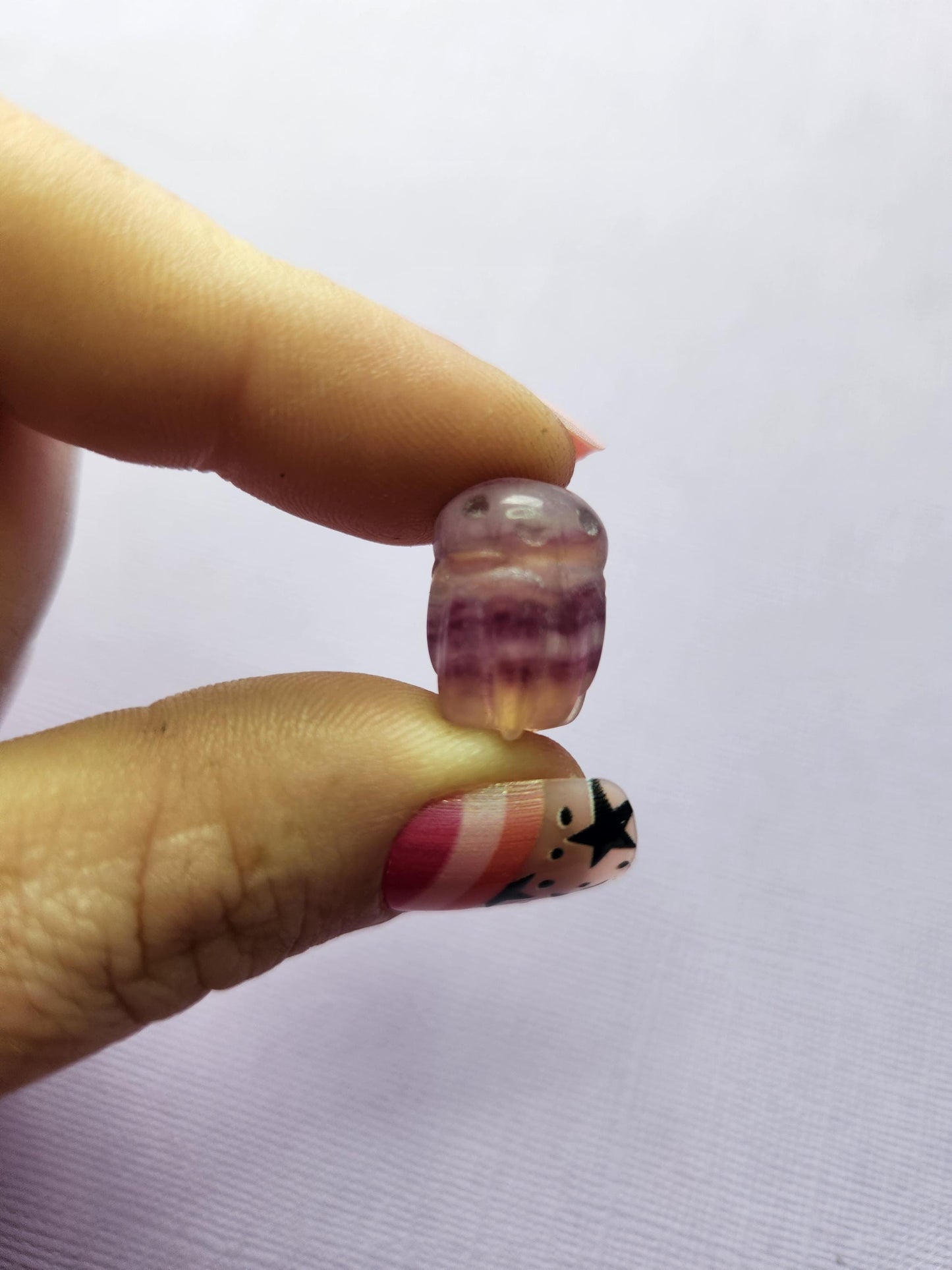 Close-up photo of a single fluorite mini octopus carving held between fingers, showing detailed tentacles and bands of purple, green and blue fluorite. Clear focus on the polished crystal octopus against a simple backdrop. Ideal for fluorite carvings, mini crystal animals, octopus crystal collectors and gemstone pocket companions