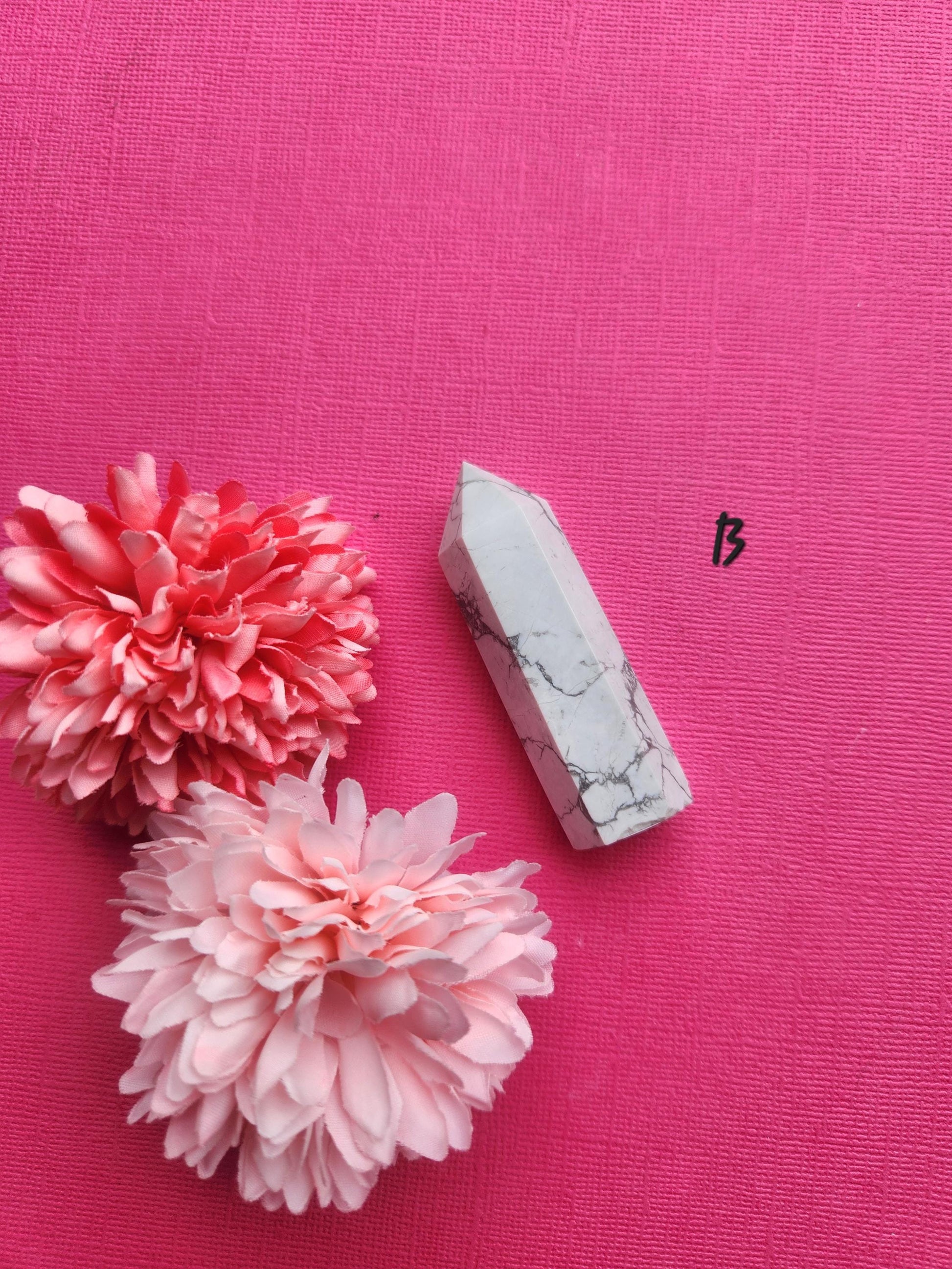 Premium Howlite crystal tower point featuring natural grey marbling, displayed on a pink backdrop with two floral props, polished Howlite generator for stress relief, grounding, spiritual healing and gemstone collection