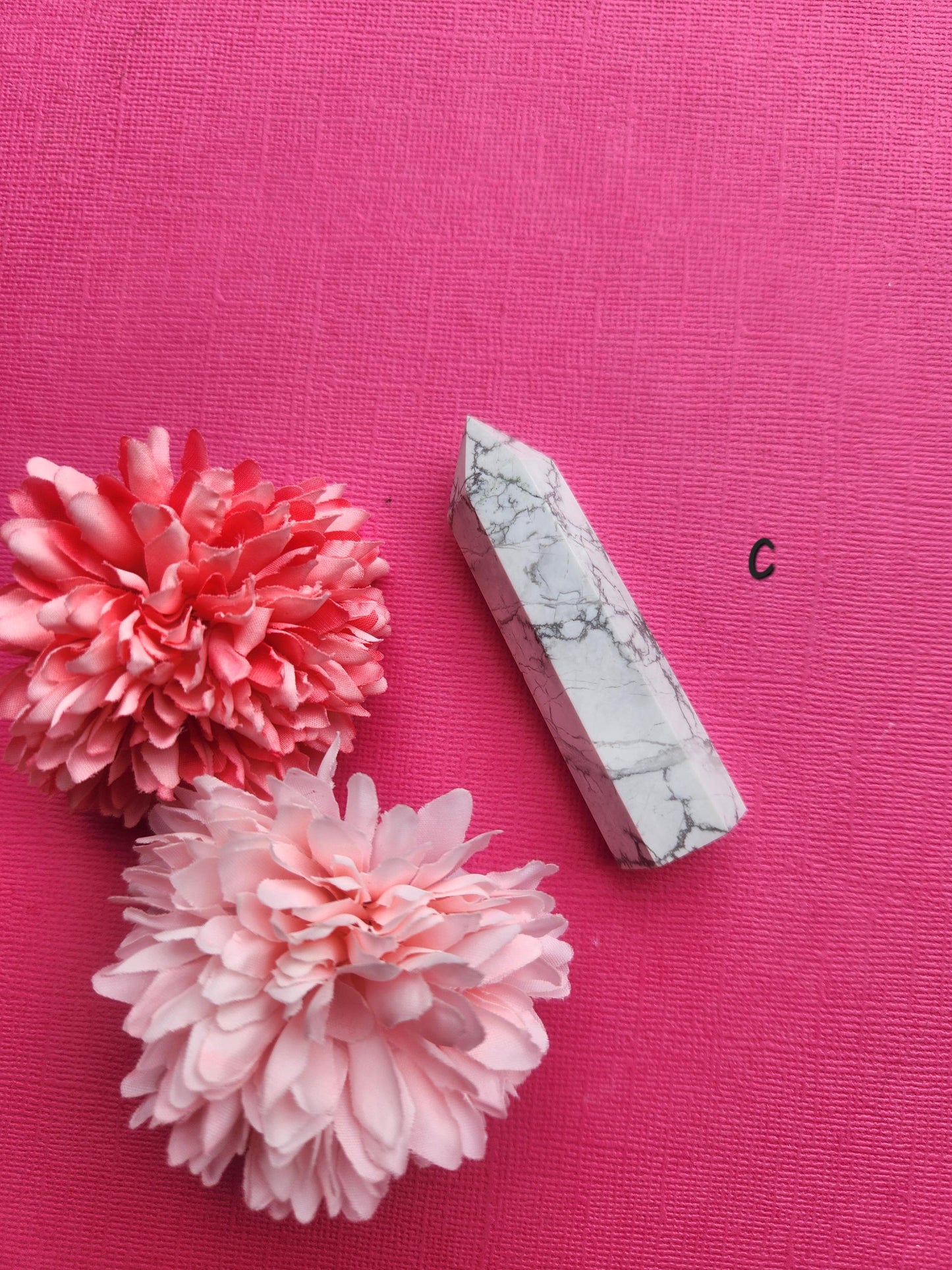 White and grey Howlite gemstone tower with smooth polished point, photographed on a pink background with two flower props, metaphysical Howlite tower for tranquillity, emotional balance, meditation and crystal décor