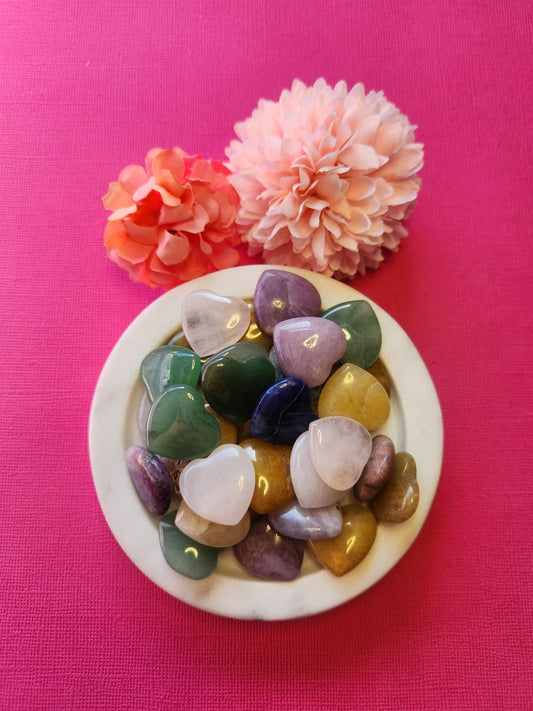 Mystery mini crystal hearts displayed on a bright pink background, featuring a variety of polished gemstones in different colors and patterns. Each heart is intuitively chosen, offering a unique surprise for crystal lovers and collectors. Perfect for pocket stones, self-love rituals, and spiritual gifts. The vibrant pink backdrop enhances the playful and loving energy of these mini heart-shaped crystals.