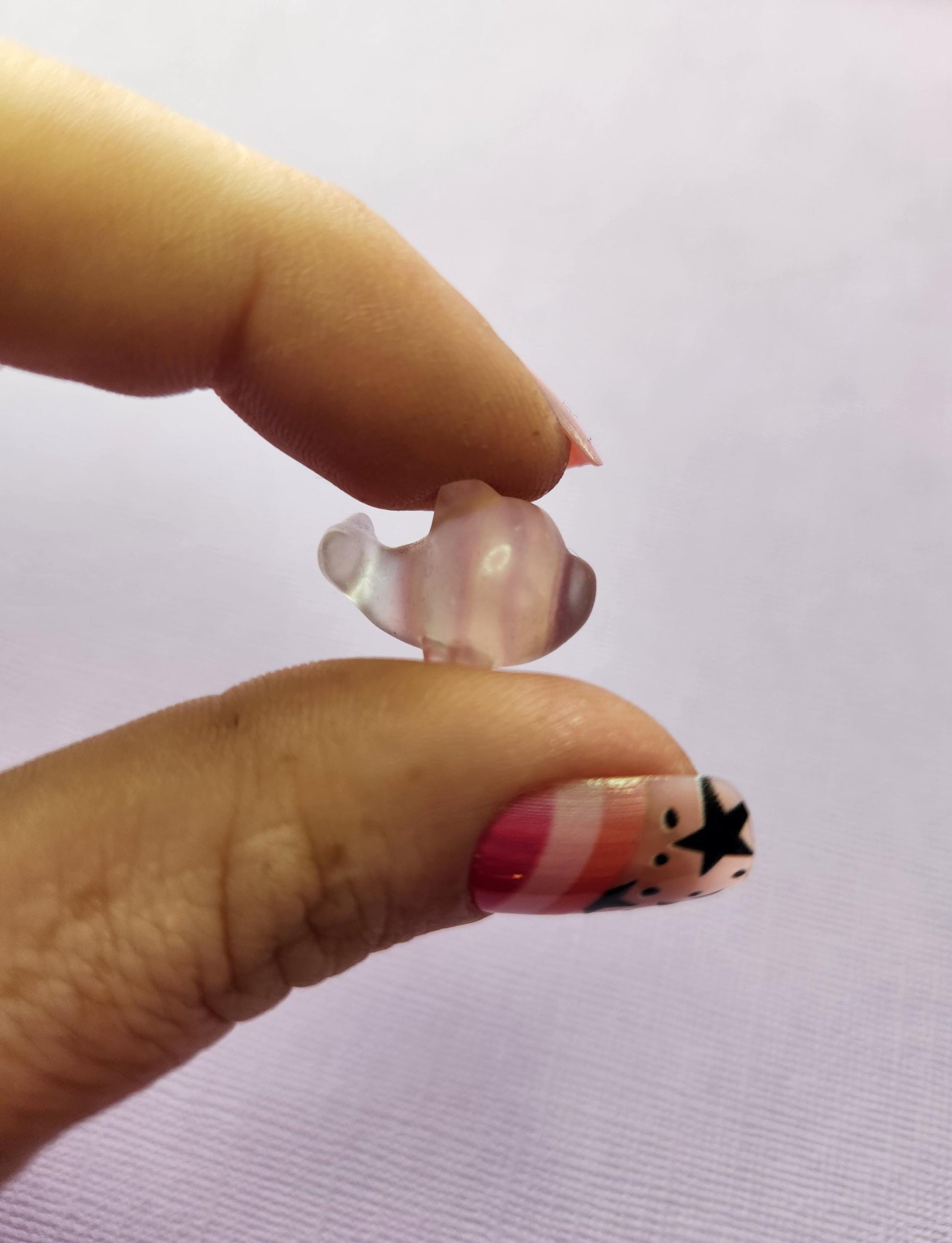Close-up photo of a single fluorite mini whale carving held between fingers, capturing the polished details and natural purple, green and blue fluorite banding against a lavender backdrop. Perfect for fluorite carvings, mini crystal animals, whale crystal collectors and pocket-sized gemstone companions