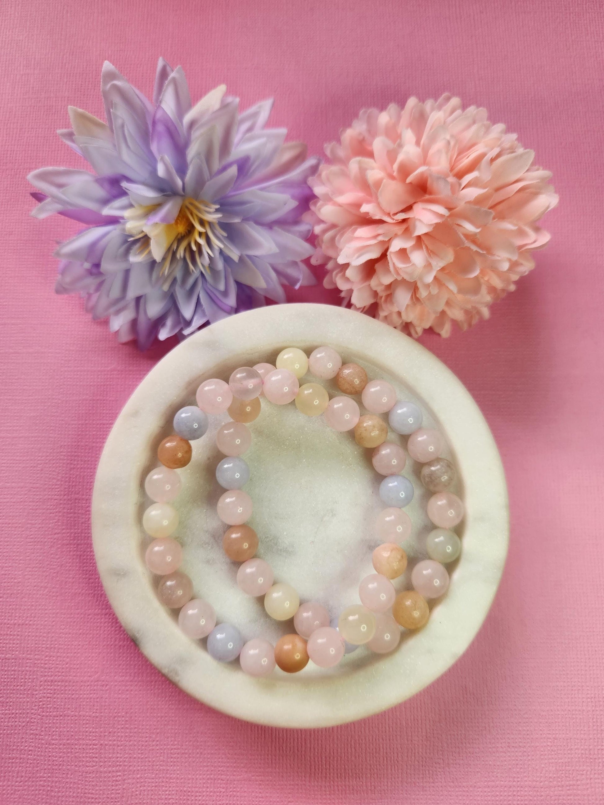 Morganite 8mm crystal bead bracelets displayed in a white dish with floral props on a pink background, natural morganite gemstone stretch bracelets for love compassion emotional healing and gentle heart energy