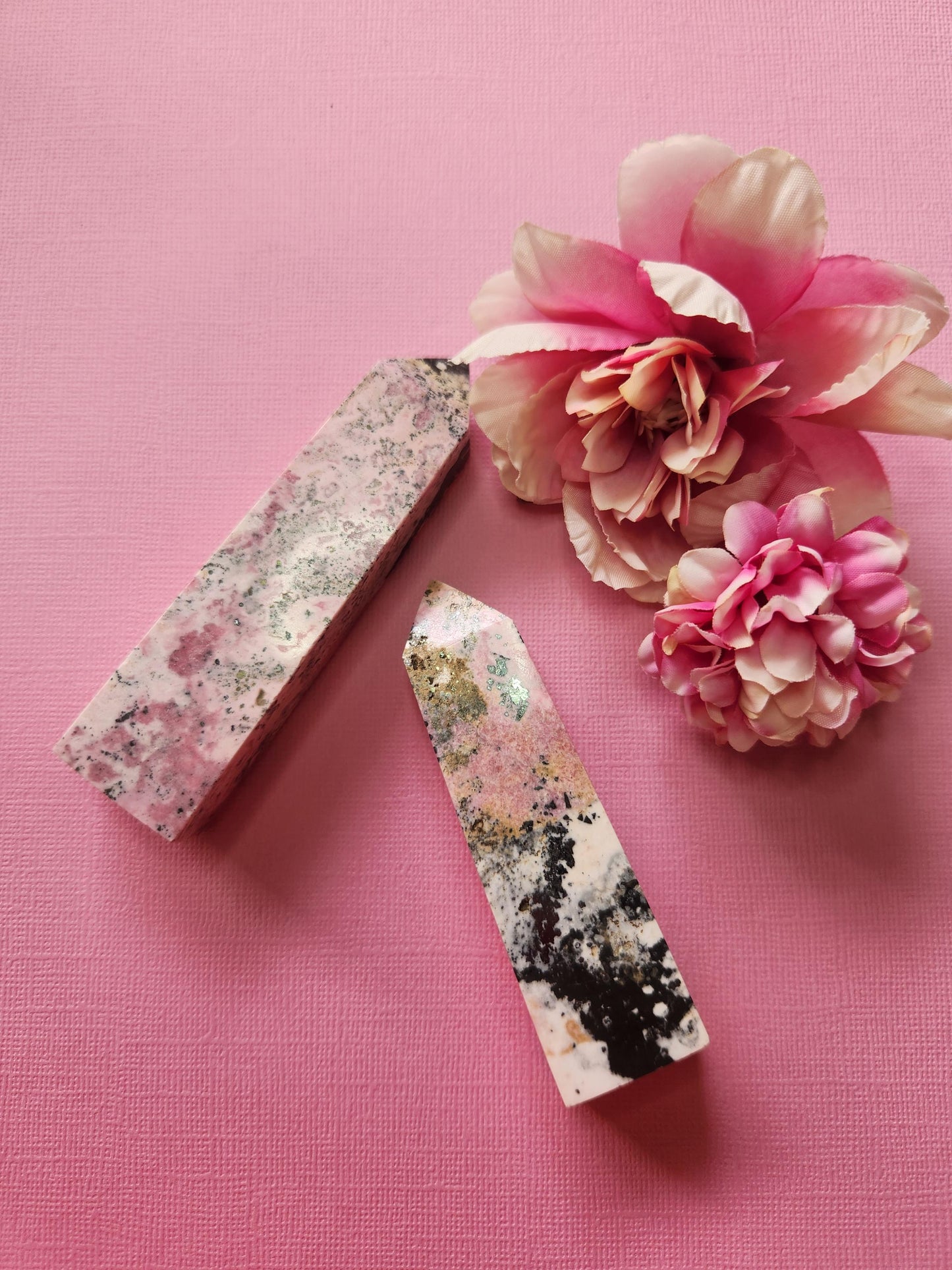 Peruvian Rhodonite crystal towers set of two with rich pink and black patterns, standing upright with two flower props on a pink background, high-quality polished rhodonite points for emotional healing, self-love crystal decor, metaphysical gemstone photography