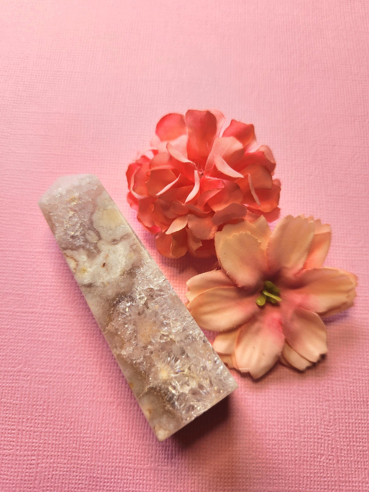 Pink Amethyst crystal tower standing upright with two delicate flower props on a light pink background, polished point for heart chakra healing, self love rituals, spiritual décor, and meditation energy work.