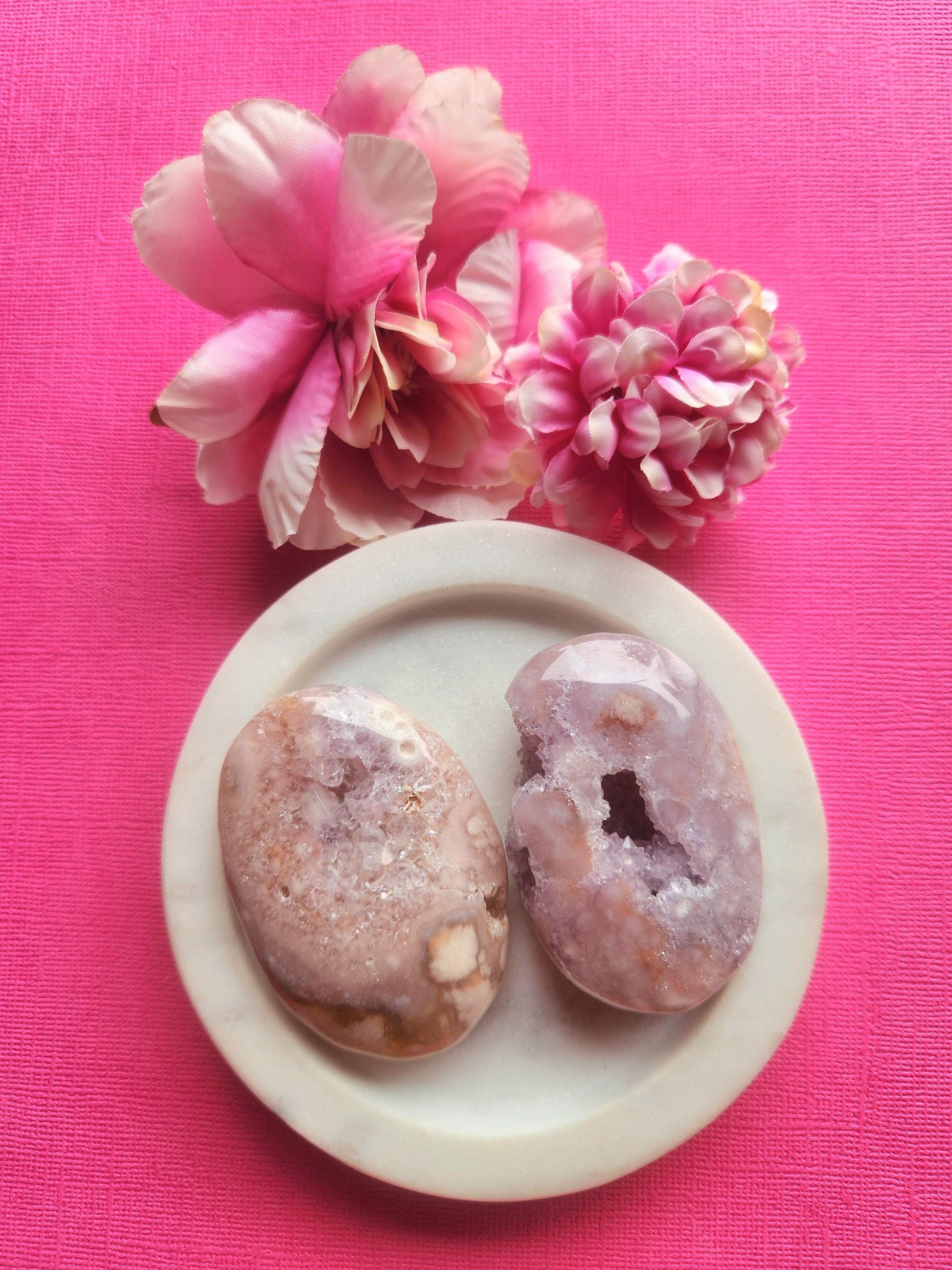 Pink amethyst druzy palmstones displayed in a white ceramic dish with two floral props on a soft pink background, featuring natural pink amethyst crystals with sparkling druzy pockets, polished healing crystal palm stones for calm intuition and emotional balance, perfect for gifting meditation altar decor and crystal collections