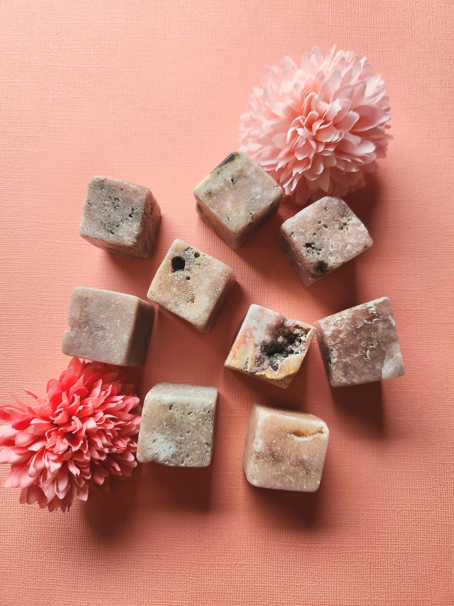 Pink amethyst cubes spread out, displaying their natural variations in color and polished texture. These healing gemstone cubes are known for promoting calm energy, spiritual balance, and meditation support. The scattered arrangement emphasizes the unique beauty of each cube, perfect for gifting or adding to a crystal collection.