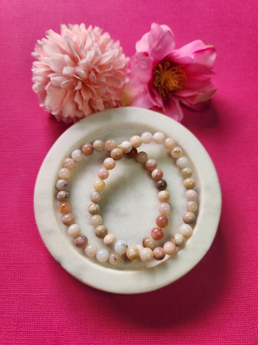 Two Pink Opal 6mm beaded bracelets displayed on a white dish with two flower props against a bright pink background. The soft pink gemstones radiate loving, heart-healing, and calming energy. Perfect for self-love, emotional balance, and crystal jewelry collections.
