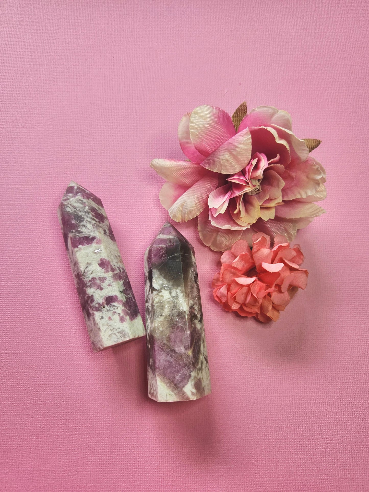 Two pink tourmaline crystal towers with rich pink mineral veining, polished gemstone points displayed with two flower props on a pink background, high-quality healing crystal decor for energy balancing, grounding and heart chakra support