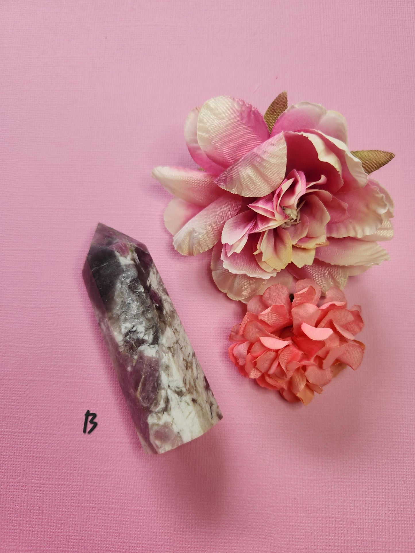 Pink tourmaline tower B featuring deep pink inclusions and natural mineral patterning, polished crystal point displayed with two flower props on a pink backdrop, premium healing crystal for heart chakra alignment, emotional healing and metaphysical use