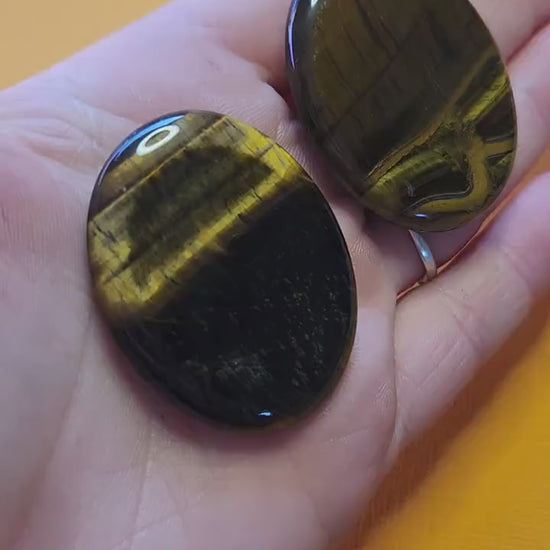 Video of two Tiger’s Eye worry stones held in hand against a yellow background, showing polished golden-brown stones with natural shimmer — grounding crystal for courage, focus, confidence, and protection.