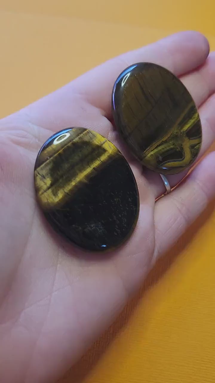 Video of two Tiger’s Eye worry stones held in hand against a yellow background, showing polished golden-brown stones with natural shimmer — grounding crystal for courage, focus, confidence, and protection.