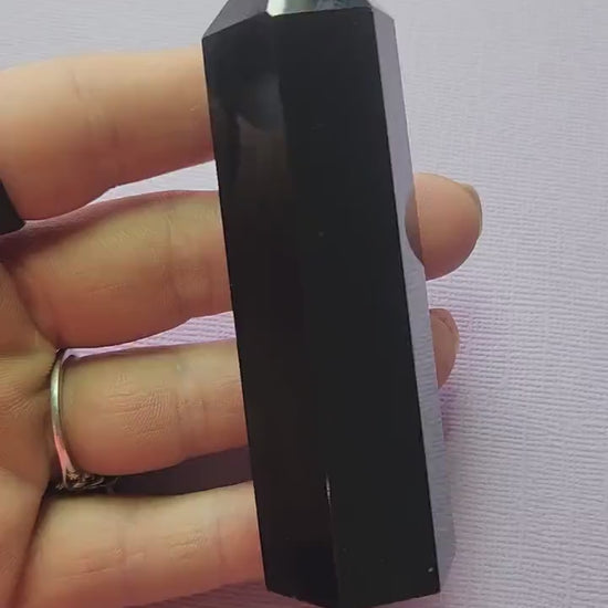 Video of polished Black Obsidian crystal tower held in hand against lavender background, showing glossy deep black surface, grounding and protection crystal point for energy clearing and shielding