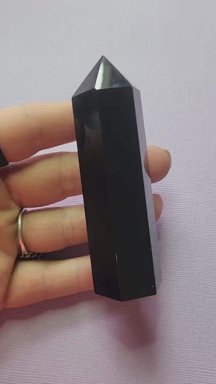 Video of polished Black Obsidian crystal tower held in hand against lavender background, showing glossy deep black surface, grounding and protection crystal point for energy clearing and shielding