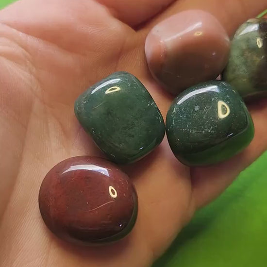 Video showcasing polished Ocean Jasper tumbles up close on a bright green background. Features natural multicolored patterns, including green, pink, and cream swirls. Perfect for crystal collectors, crystal healing, and gemstone enthusiasts