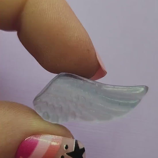 Close-up video of a single fluorite mini wing carving held in hand, highlighting the polished details and natural purple, green and blue fluorite banding as it catches the light against a lavender backdrop. Ideal for fluorite carvings, angel wing crystals and collectible gemstone accents