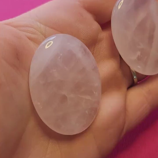 Video of a hand holding polished Rose Quartz worry stones against a bright pink background, highlighting their soft pink color and smooth finish — ideal for emotional healing, stress relief, meditation, and crystal energy work.