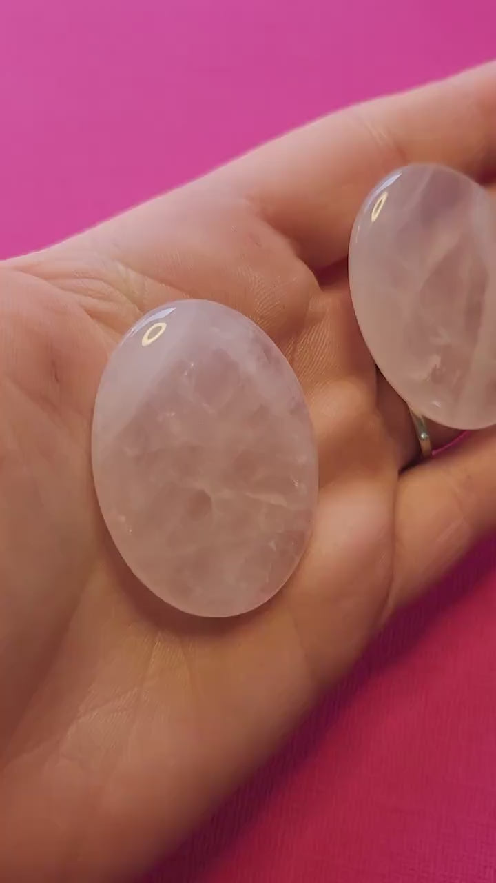 Video of a hand holding polished Rose Quartz worry stones against a bright pink background, highlighting their soft pink color and smooth finish — ideal for emotional healing, stress relief, meditation, and crystal energy work.