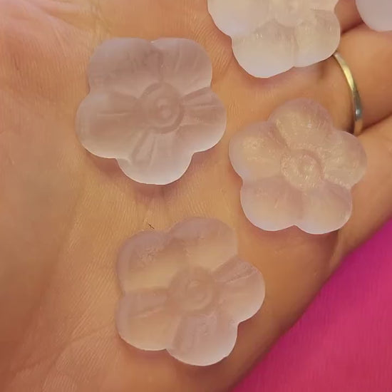 Video of a hand holding Selenite flower carvings against a pink background, showing their soft white glow and petal detailing — perfect for energy cleansing, meditation, and crystal decor.