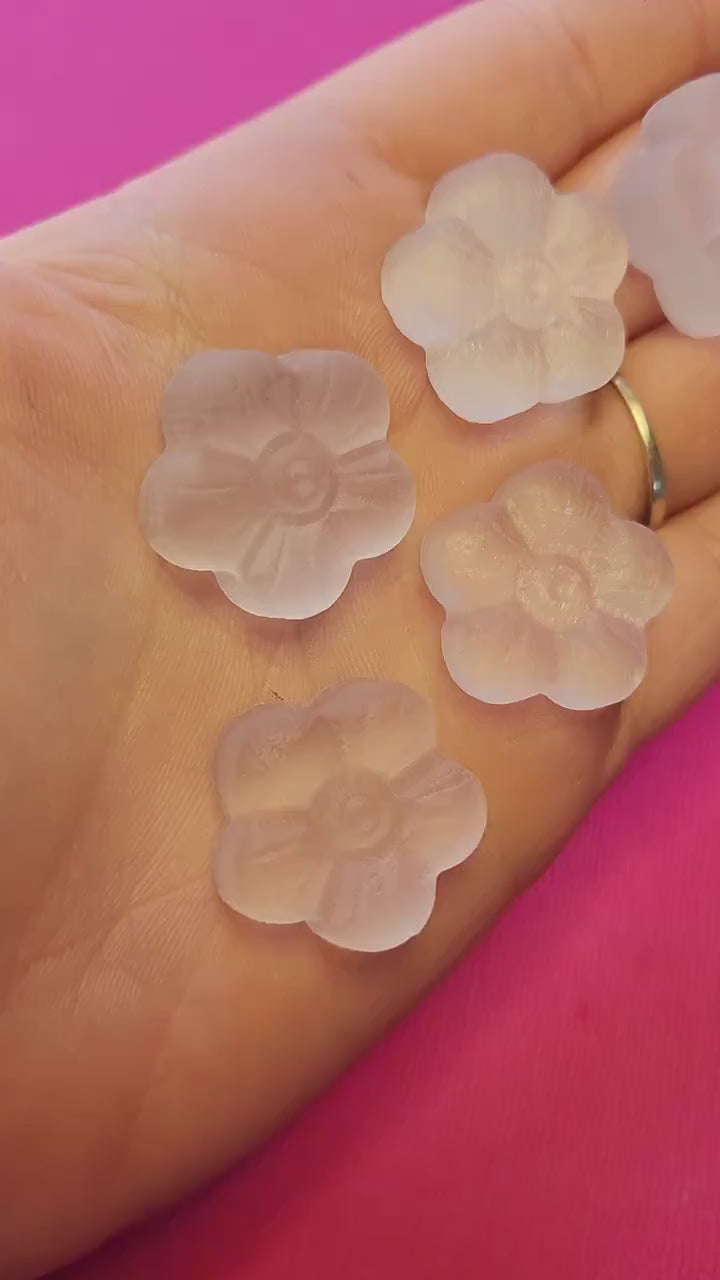 Video of a hand holding Selenite flower carvings against a pink background, showing their soft white glow and petal detailing — perfect for energy cleansing, meditation, and crystal decor.