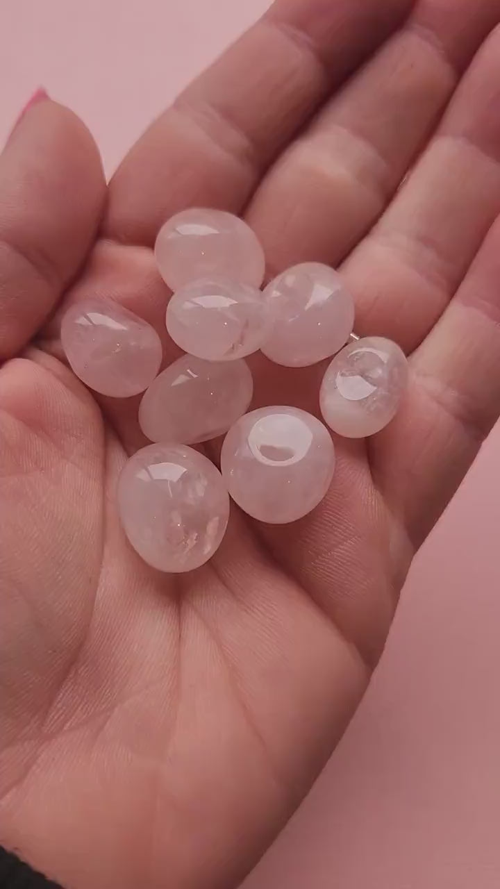 Video of a hand holding polished Rose Quartz tumbles against a light pink background, highlighting their soft pink color and smooth finish — ideal for love, emotional healing, and crystal energy work.