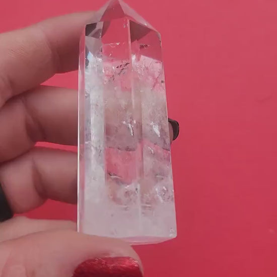Close-up video of a polished Clear Quartz tower held in hand against a red background, showcasing natural clear quartz clarity and crystal structure, high-vibration healing crystal point for energy amplification, meditation, spiritual growth, chakra balancing, manifestation, Reiki, home altar décor, and metaphysical crystal collection